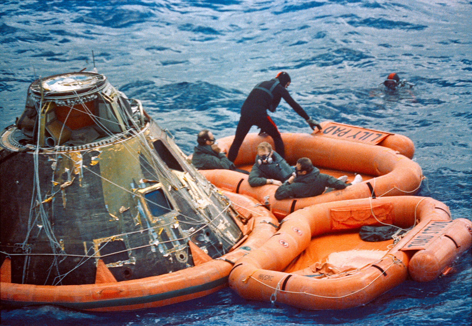 A photo of astronauts Mitchell,Shepard,and Roosa, and a frogman on a raft