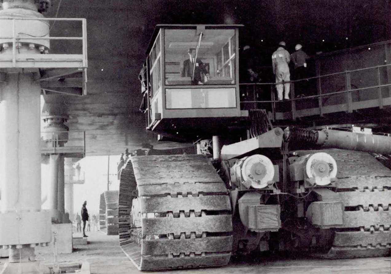 A photo of a driver eases the crawler beneath a Mobile Launcher